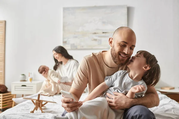Focus on joyful father and his little son having fun next to his blurred wife and baby on backdrop — Stock Photo