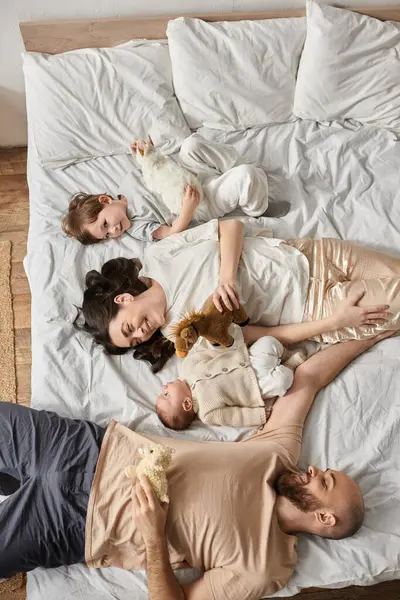 Blick von oben auf eine schöne, fröhliche Familie, die auf ihrem Bett liegt und einander anlächelt, moderne Elternschaft — Stockfoto