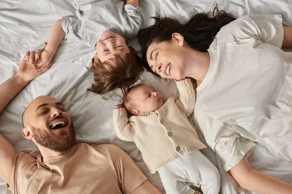 Вид на счастливую расслабляющую семью в уютной домашней одежде, лежащей на кровати вместе, современное воспитание — стоковое фото
