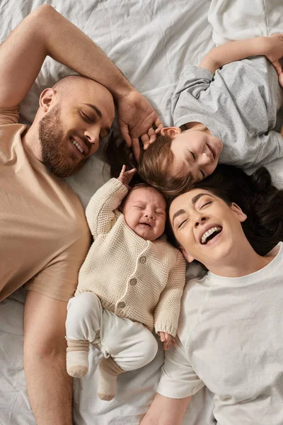 Vista superior de padres felices acostados en la cama con su pequeño hijo y bebé recién nacido, concepto de familia - foto de stock