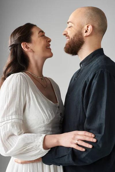 Élégant couple aimant étreignant et souriant à l'autre posant joyeusement ensemble sur fond gris — Photo de stock