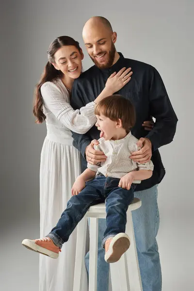 Padres modernos alegres abrazando con su sentarse en la silla alta delante de ellos, concepto de familia - foto de stock