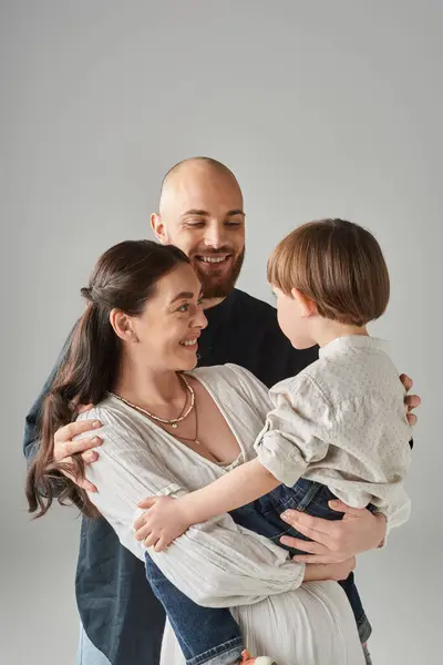 Genitori attraenti gioiosi guardando amorevolmente il loro figlio in età prescolare su sfondo grigio, famiglia — Foto stock