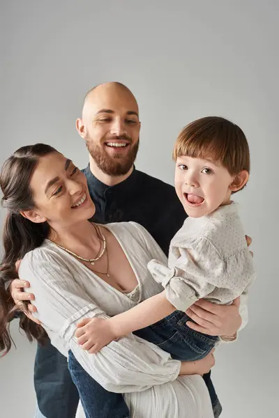 Giocoso bambino guardando la fotocamera con la bocca aperta mentre i suoi genitori lo tengono in braccio, concetto di famiglia — Foto stock