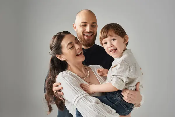 Playful little boy sticking out his tongue at camera while his cheerful parents holding him, family — Stock Photo