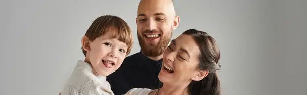 Juguetón niñito sobresaliendo de su lengua mientras sus alegres padres lo sostenían, estandarte familiar - foto de stock