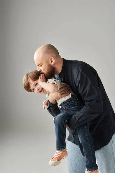 Vertical shot of happy bearded father holding and kissing his playful jolly son, modern parenting — Stock Photo