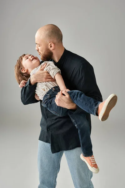 Feliz barbudo padre y su pequeño hijo tener gran tiempo juntos en gris telón de fondo, concepto de familia - foto de stock