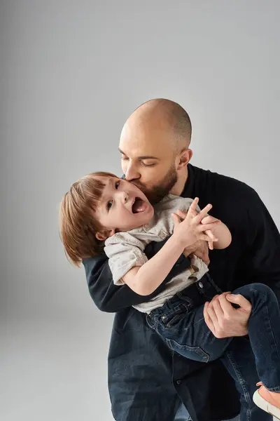 Vertical shot of bearded father kissing his joyful happy little son in cheek, modern parenting — Stock Photo