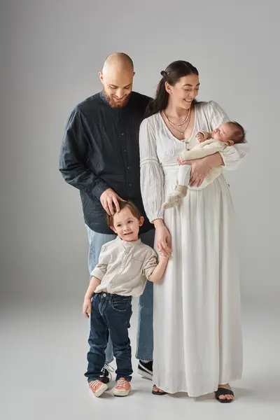 Tiro vertical de padres felices modernos posando con sus hijos pequeños sobre fondo gris - foto de stock