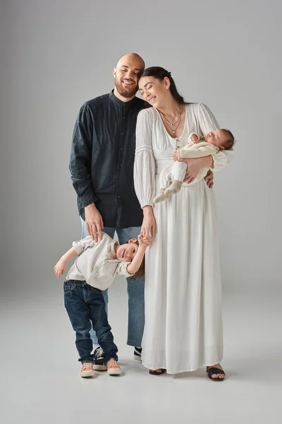 Pais modernos felizes em trajes elegantes sorrindo e posando com seus filhos em pano de fundo cinza — Fotografia de Stock