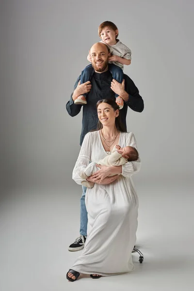 Cheerful family of four wearing classy stylish outfits and posing together on gray backdrop — Stock Photo