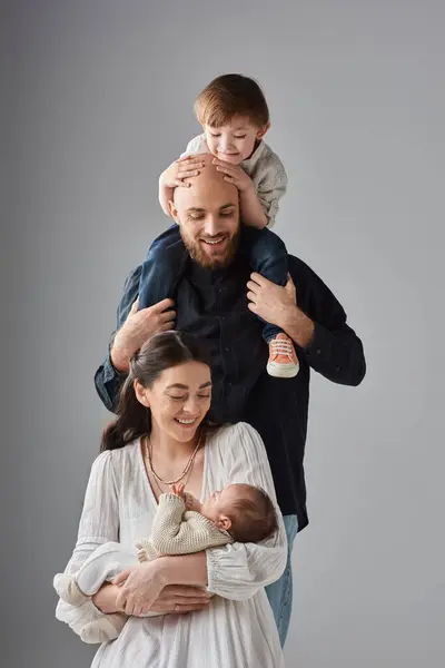 Pai barbudo segurando seu filhinho nos ombros e sorrindo para sua esposa e bebê recém-nascido, família — Fotografia de Stock