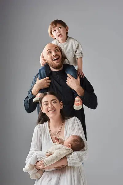 Cheerful mother sitting with baby with her husband holding their little son on shoulders behind her — Stock Photo