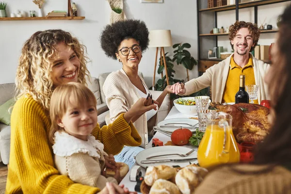 Freudige multiethnische Familie sitzt Händchenhaltend und betet am Erntedanktisch, dankbar für das Essen — Stockfoto