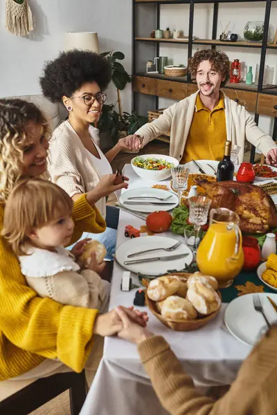 Freudige multirassische Familie hält Händchen und betet am Thanksgiving-Tisch, dankbar für das Abendessen — Stockfoto