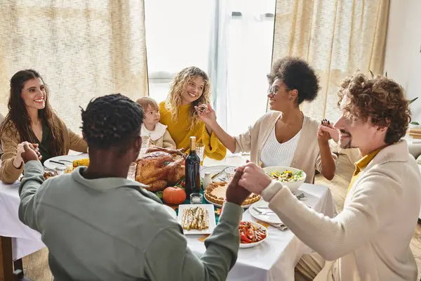 Allegri amici multirazziali e familiari che si tengono per mano e pregano al tavolo del Ringraziamento, giorno del tacchino — Foto stock
