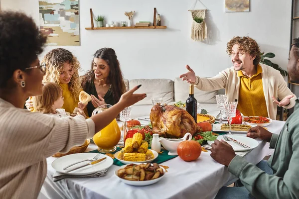 Glückliche multirassische Familie, die sich rege unterhält und am Thanksgiving-Tisch mit Truthahn gestikuliert — Stockfoto