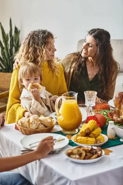 Happy lgbt family talking near toddler girl during Thanksgiving celebration, festive dinner — Stock Photo