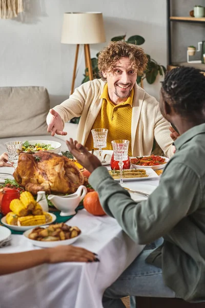 Happy multicultural men talking near roasted turkey on Thanksgiving day, feast and gathering — Stock Photo