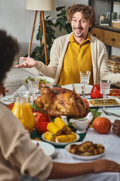 Feliz hombre haciendo gestos y hablando durante la cena de Acción de Gracias en círculo familiar, pavo asado en la mesa - foto de stock