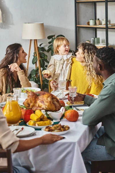 Празднование Дня Благодарения, счастливая межрасовая семья смотрит на малышку возле праздничного стола — стоковое фото