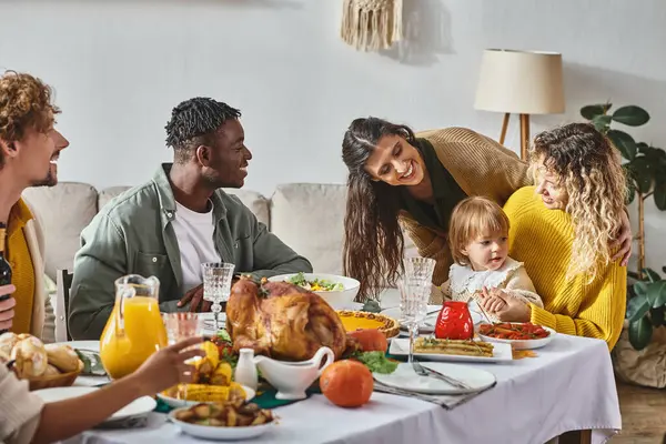 Happy interracial people looking at cute toddler baby during Thanksgiving celebration at home — Stock Photo