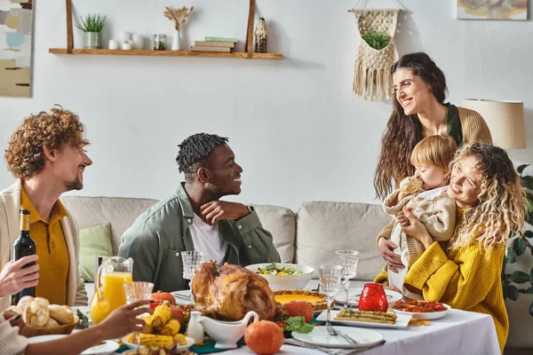 Happy lesbian couple hugging toddler baby and smiling during Thanksgiving celebration at home — Stock Photo