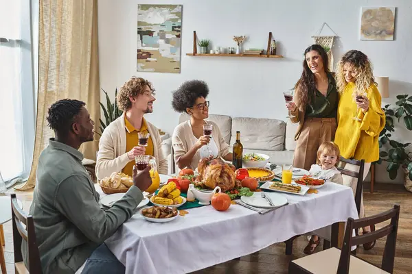 Familia interracial disfrutando de la cena de Acción de Gracias, niño feliz sentado cerca de padres lgbt - foto de stock