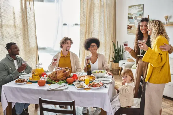 Amigos multiculturales que celebran el Día de Acción de Gracias con la familia lgbt y la niña pequeña, reuniéndose - foto de stock