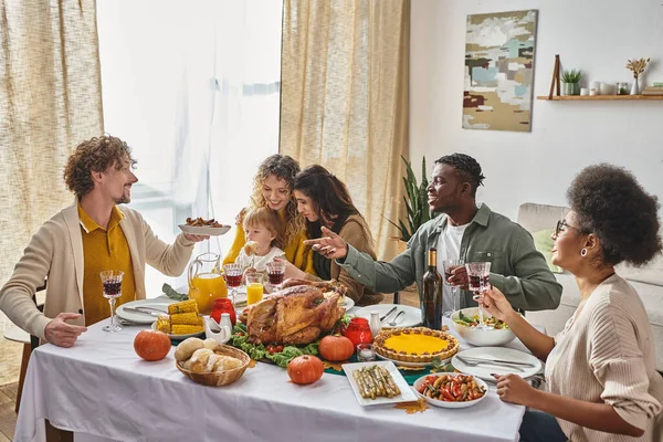 Happy man passing plate with roasted potatoes to african american friend during Thanksgiving dinner — Stock Photo