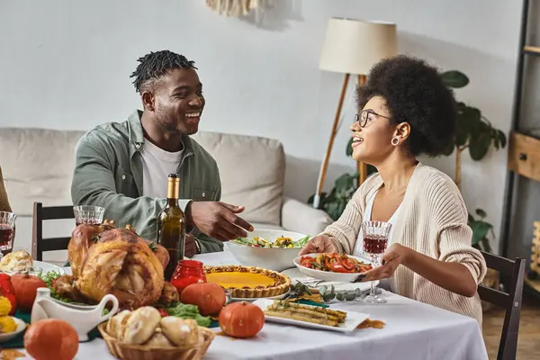 Happy african american woman passing plate with cooked meal to relative during Thanksgiving dinner — Stock Photo