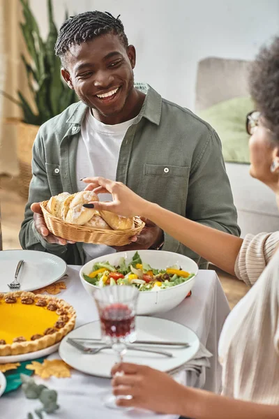 Happy african american man looking at sister taking baked bun during Thanksgiving holiday — Stock Photo