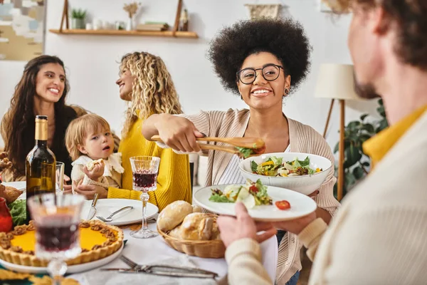 Happy african american woman serving salad to curly man on Thanksgiving day, lgbt family and baby — Stock Photo