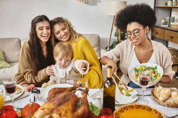 Fröhliche afrikanisch-amerikanische Frau serviert Salat neben lesbischem Paar und Baby am Thanksgiving-Tag — Stockfoto
