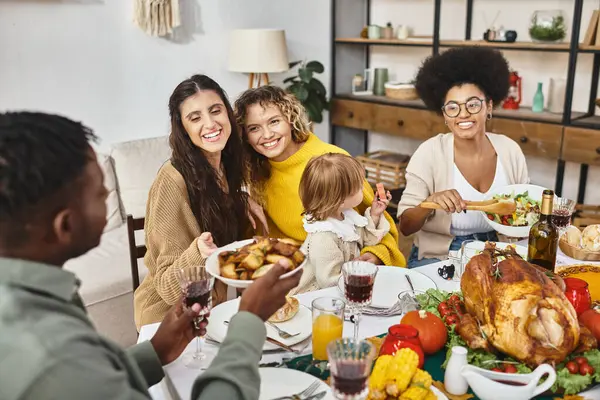 Amigos multiculturales felices y familia lgbt compartir comida mientras celebran Acción de Gracias juntos - foto de stock
