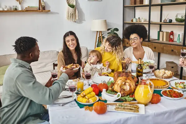 Amigos multiétnicos alegres o miembros de la familia que comparten la comida mientras celebran Acción de Gracias juntos - foto de stock