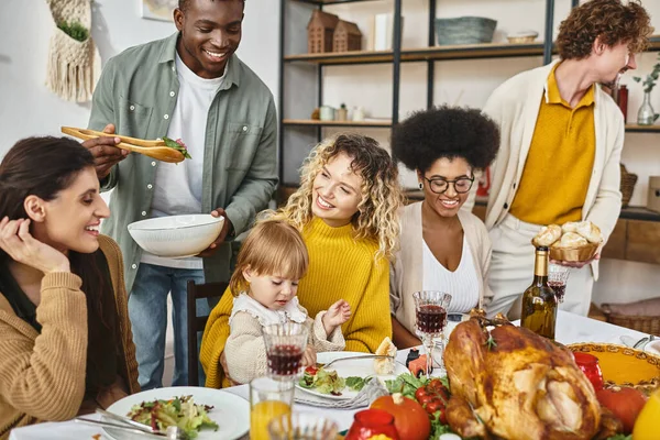Fiesta de Acción de Gracias, amigos multiétnicos positivos y reunión familiar en la mesa festiva con pavo - foto de stock