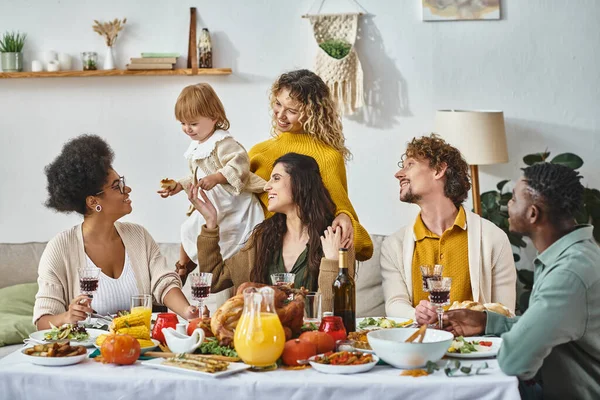 Feliz Día de Acción de Gracias, alegres amigos multiculturales y reunión familiar en la mesa festiva con pavo - foto de stock