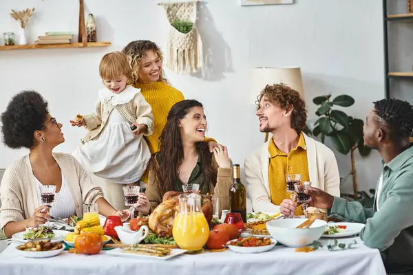 Feliz Día de Acción de Gracias, alegres amigos multiculturales y reunión familiar en la mesa con pavo asado - foto de stock