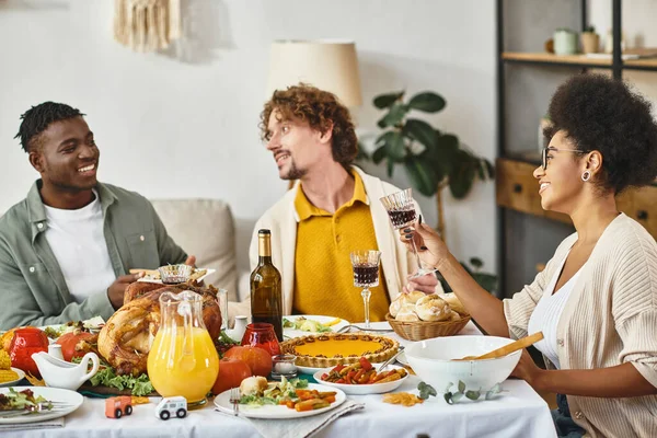 Thanksgiving tradition, cheerful multiethnic friends chatting at feasting table with roasted turkey — Stock Photo