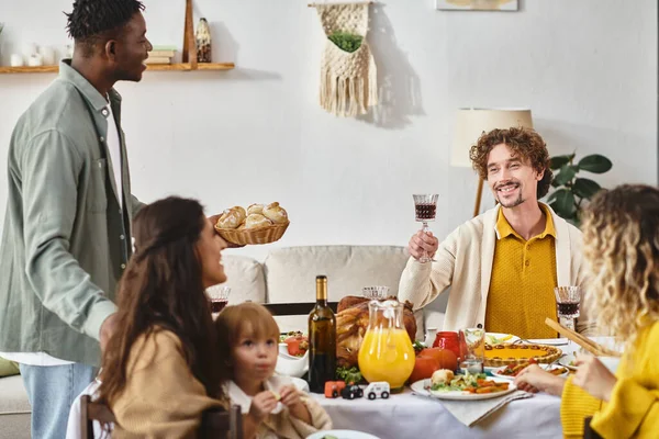 Cheerful man toasting with glass of red wine near multicultural friends and family on Thanksgiving — Stock Photo