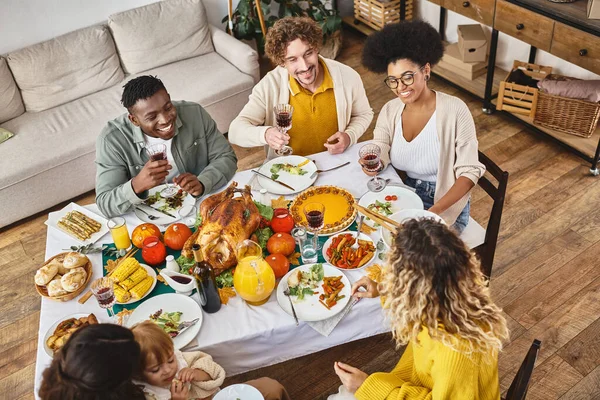 Feliz Acción de Gracias, alegres amigos interracial y reunión familiar en la mesa festiva con pavo - foto de stock
