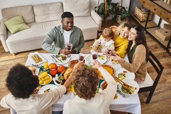 Feliz Día de Acción de Gracias, sonrientes amigos multiétnicos y familiares tintineo vasos de vino, vista superior - foto de stock