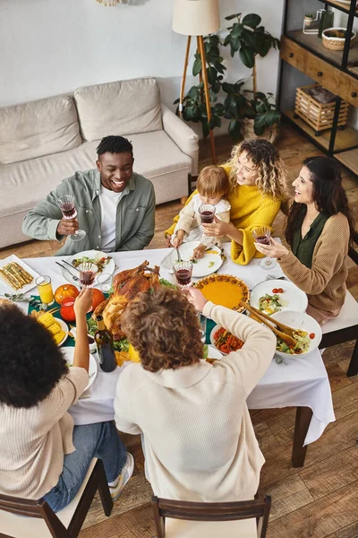 Feliz Día de Acción de Gracias, sonrientes amigos multiétnicos y familiares animando cerca de pavo asado, vista superior - foto de stock
