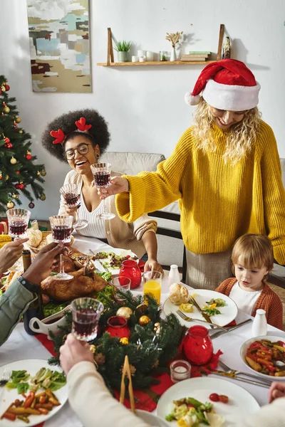Heureux amis multiethniques et la famille en chapeaux Santa acclamant lunettes tout en célébrant Noël — Photo de stock