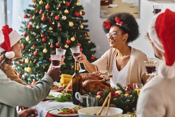 Concepto de vacaciones de invierno, alegres mujeres multiétnicas tintineando gafas y celebrando la Navidad - foto de stock