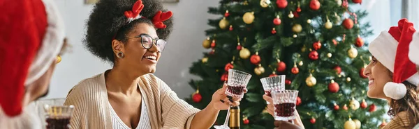 Winter holidays banner, cheerful multiethnic women clinking glasses and celebrating Christmas — Stock Photo