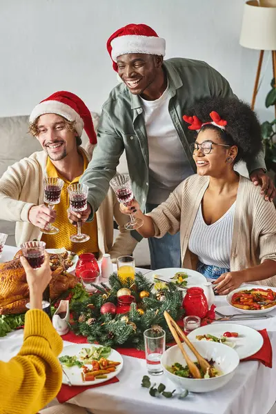 Allegri parenti multietnici in abbigliamento casual con cappelli di Babbo Natale che si tintinnano gli occhiali, Natale — Foto stock