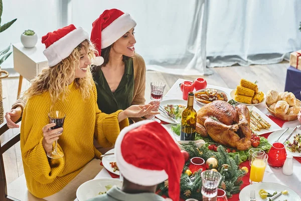 Alegre pareja lgbt sentado en la mesa de Navidad junto con su familia multiétnica hablando alegremente - foto de stock